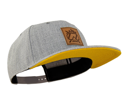 Ski Snapback Cap von Jumping Bird - Modell Sölden in hellgrau/gelb mit Badge in Lederoptik und Logo-Stick seitlich