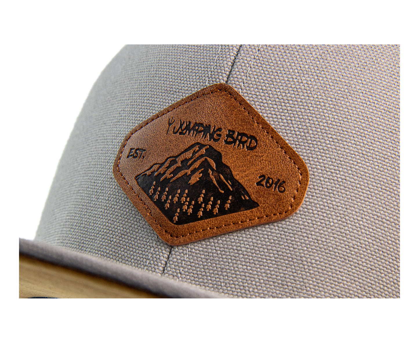 Snapback Cap von Jumping Bird - Modell Aletschhorn in hellgrau mit Badge in Lederoptik und Logo-Stick seitlich