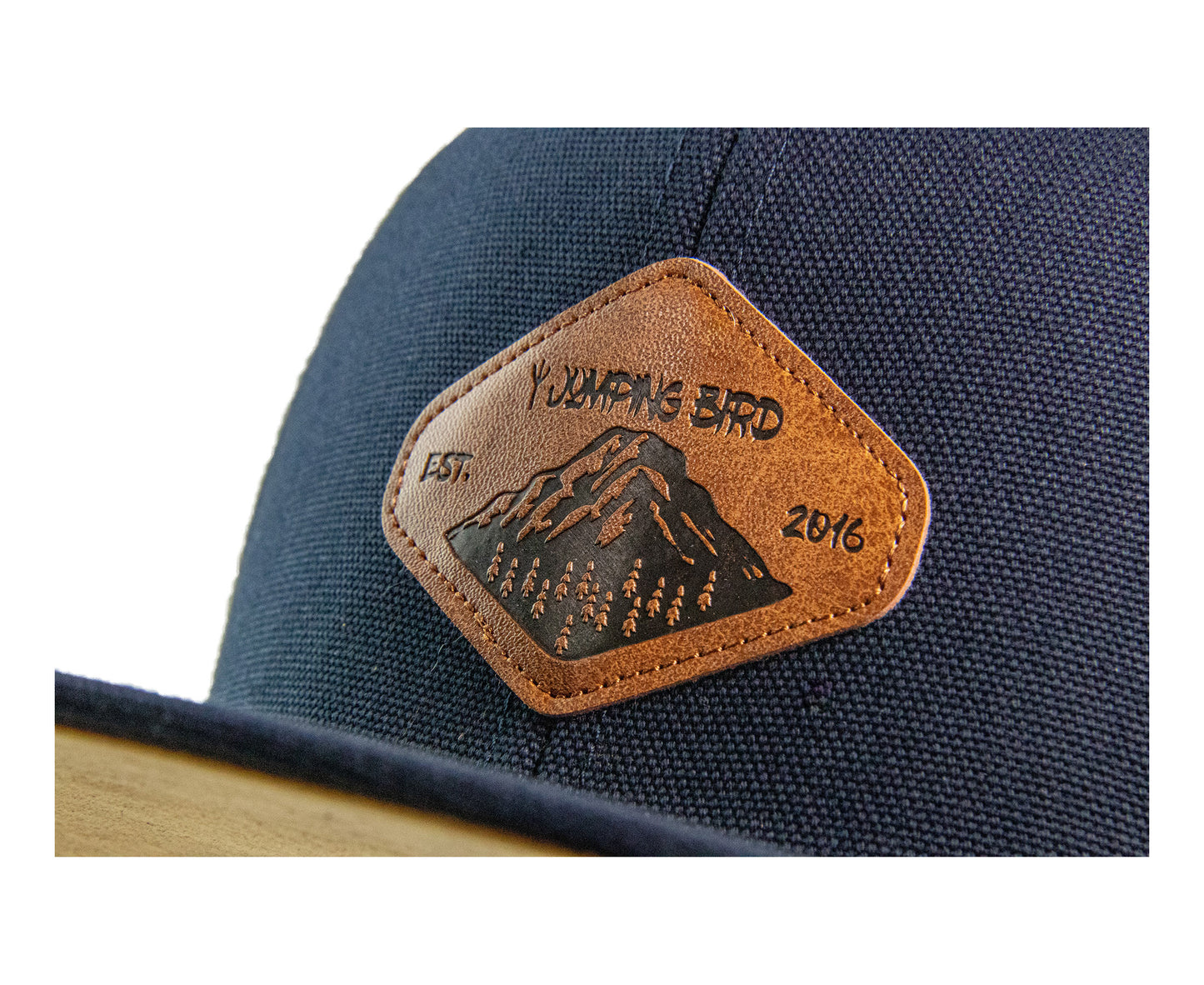 Snapback Cap von Jumping Bird - Modell Dom in dunkelblau mit Badge in Lederoptik und Logo-Stick seitlich