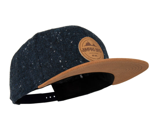 Snapback-Cap von Jumping Bird in Anthrazitblau-Braun mit geprägtem Lederoptik-Patch vorn und seitlichem Logostick