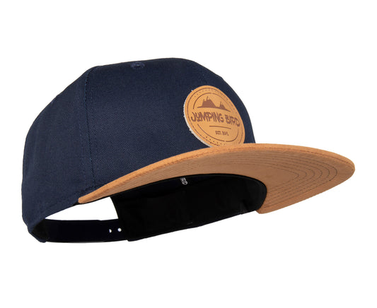Snapback-Cap von Jumping Bird in Ozeanblau-Braun mit geprägtem Lederoptik-Patch vorn und seitlichem Logostick