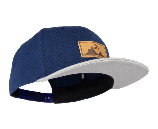 Snapback-Cap von Jumping Bird in Blau-Grau mit geprägtem Lederoptik-Patch vorn und seitlichem Logostick