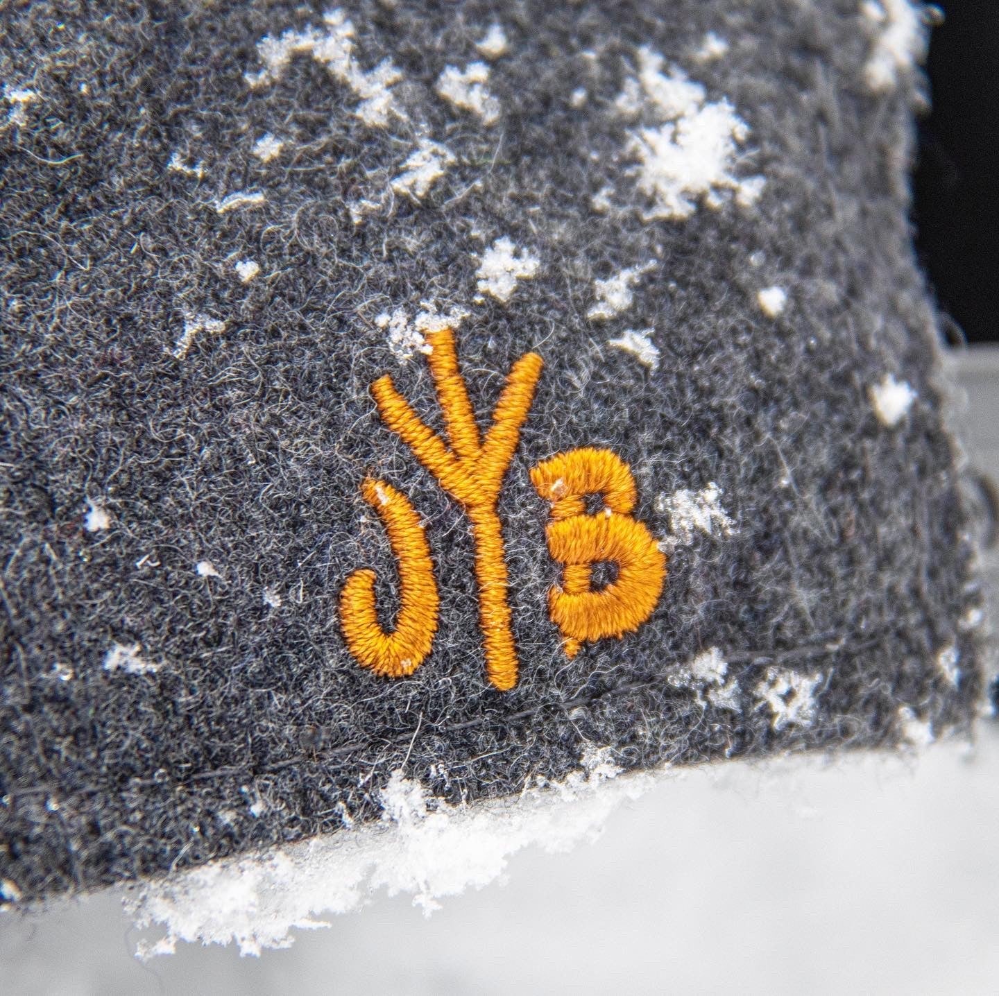 Snowboard Snapback Cap von Jumping Bird - Modell Leogang in dunkelgrau/orange mit Badge in Lederoptik und Logo-Stick seitlich