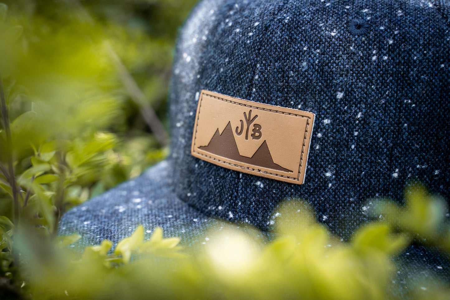 Snapback-Cap von Jumping Bird in Anthrazitblau meliert mit geprägtem Lederoptik-Patch vorn und seitlichem Logostick