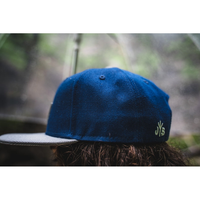 Snapback-Cap von Jumping Bird in Blau-Grau mit geprägtem Lederoptik-Patch vorn und seitlichem Logostick