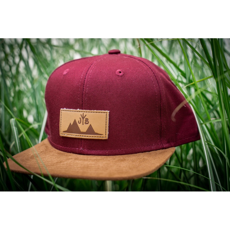 Snapback-Cap von Jumping Bird in Bordeaux-Braun mit geprägtem Lederoptik-Patch vorn und seitlichem Logostick