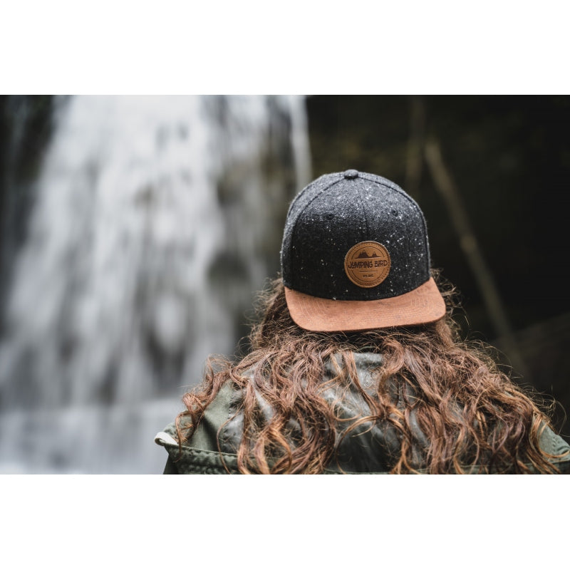Snapback-Cap von Jumping Bird in Dunkelgrau-Braun mit geprägtem Lederoptik-Patch vorn und seitlichem Logostick