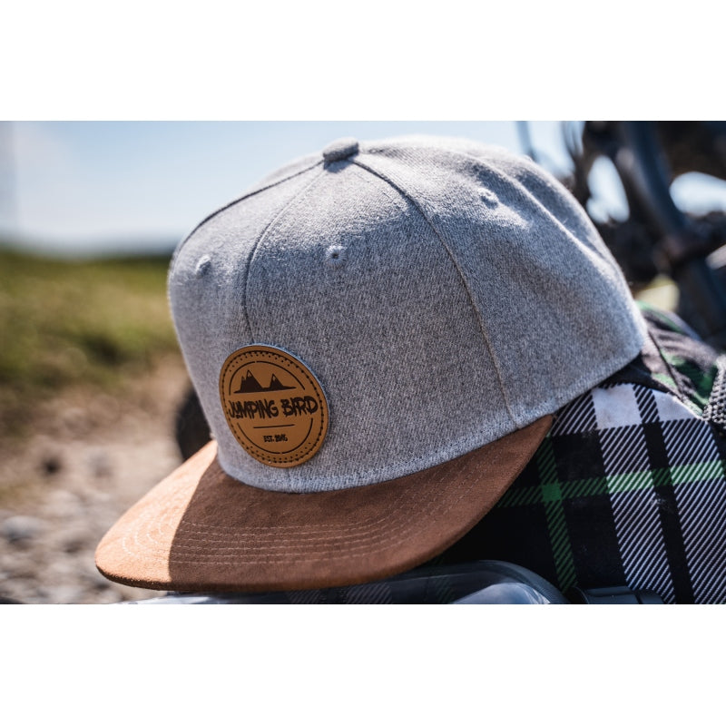 Snapback-Cap von Jumping Bird in Hellgrau meliert/Braun mit geprägtem Lederoptik-Patch vorn und seitlichem Logostick