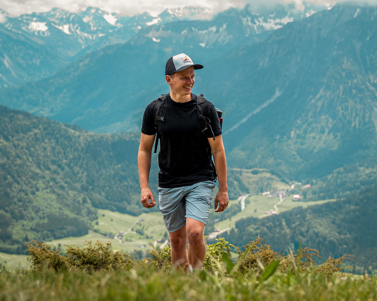 Mann mit Jumping Bird Cap beim Wandern in den Bergen