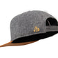 Filz-Snapback von Jumping Bird in Steingrau-Braun mit geprägtem Lederoptik-Patch vorn und seitlichem Logostick