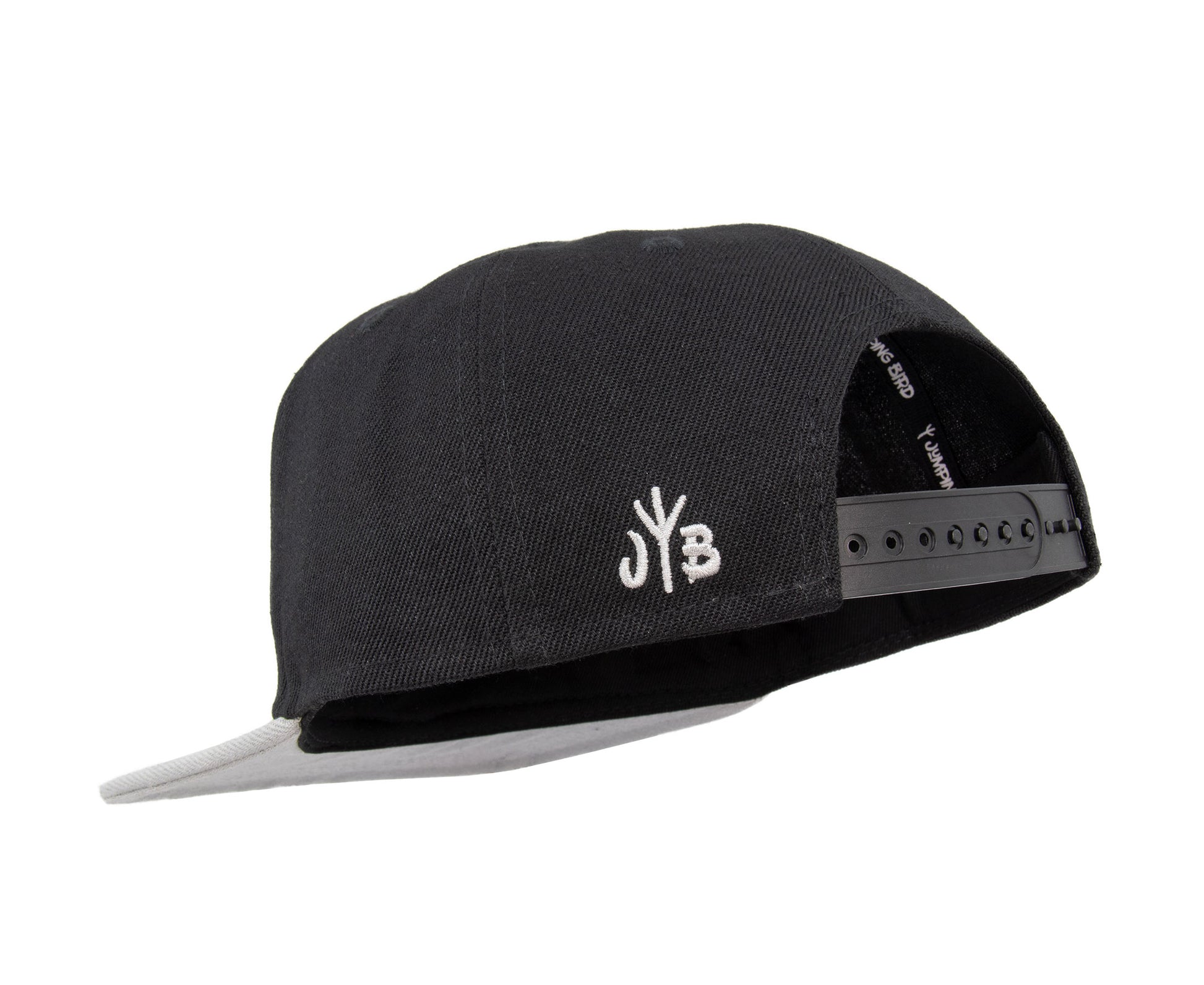 Snapback-Cap von Jumping Bird in Schwarz-Grau mit geprägtem Lederoptik-Patch vorn und seitlichem Logostick