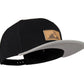 Snapback-Cap von Jumping Bird in Schwarz-Grau mit geprägtem Lederoptik-Patch vorn und seitlichem Logostick