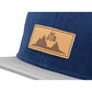 Snapback-Cap von Jumping Bird in Blau-Grau mit geprägtem Lederoptik-Patch vorn und seitlichem Logostick