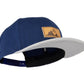 Snapback-Cap von Jumping Bird in Blau-Grau mit geprägtem Lederoptik-Patch vorn und seitlichem Logostick