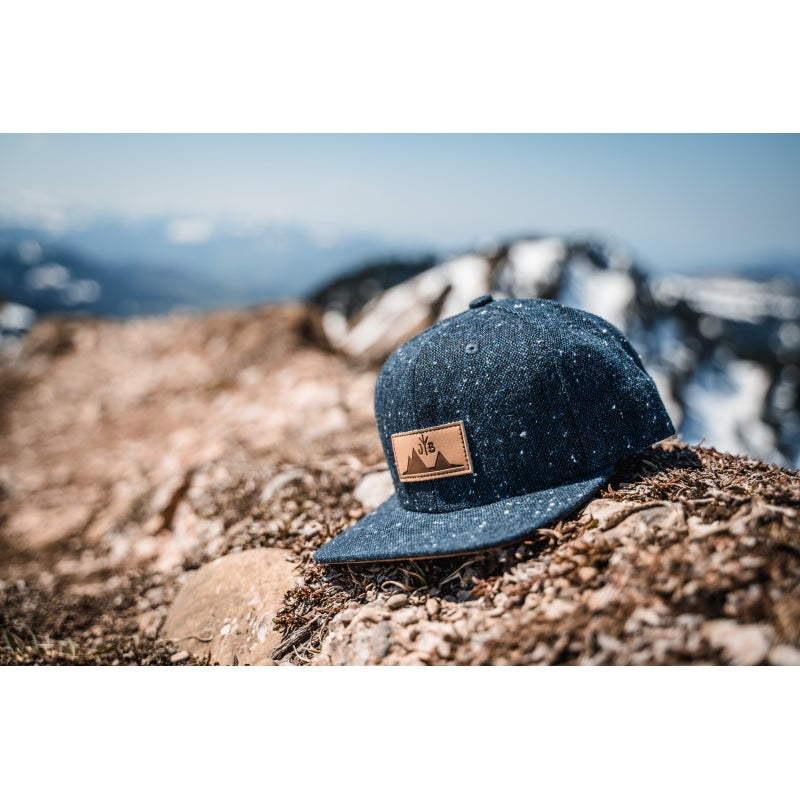 Snapback-Cap von Jumping Bird in Anthrazitblau meliert mit geprägtem Lederoptik-Patch vorn und seitlichem Logostick