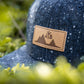 Snapback-Cap von Jumping Bird in Anthrazitblau meliert mit geprägtem Lederoptik-Patch vorn und seitlichem Logostick