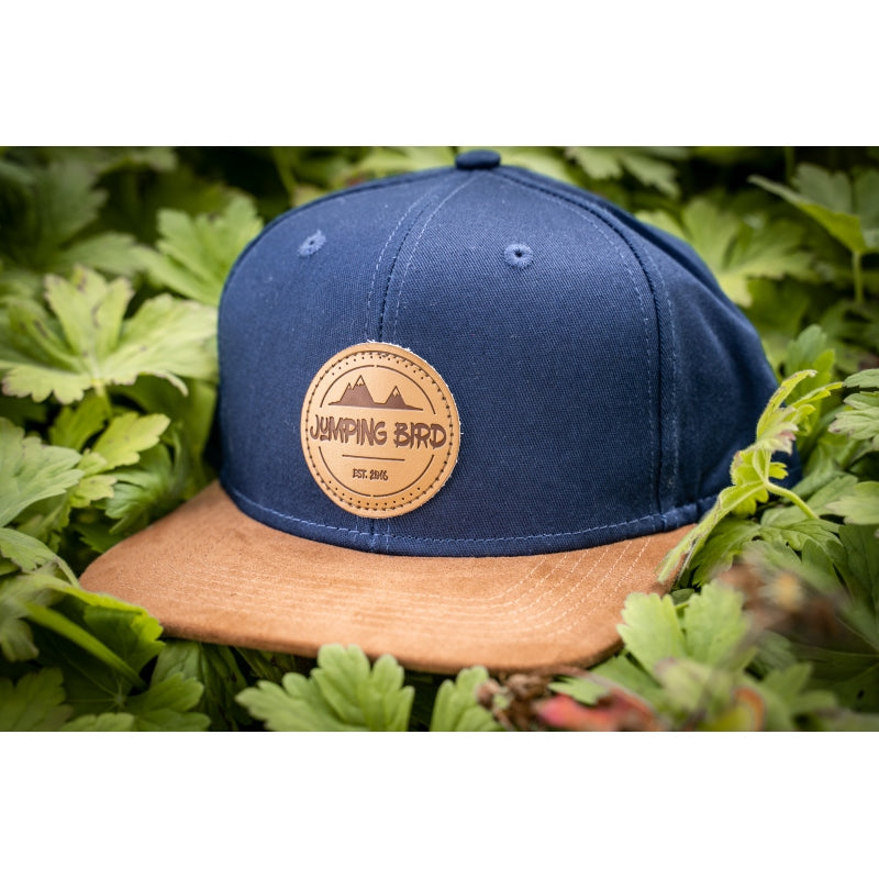 Snapback-Cap von Jumping Bird in Ozeanblau-Braun mit geprägtem Lederoptik-Patch vorn und seitlichem Logostick