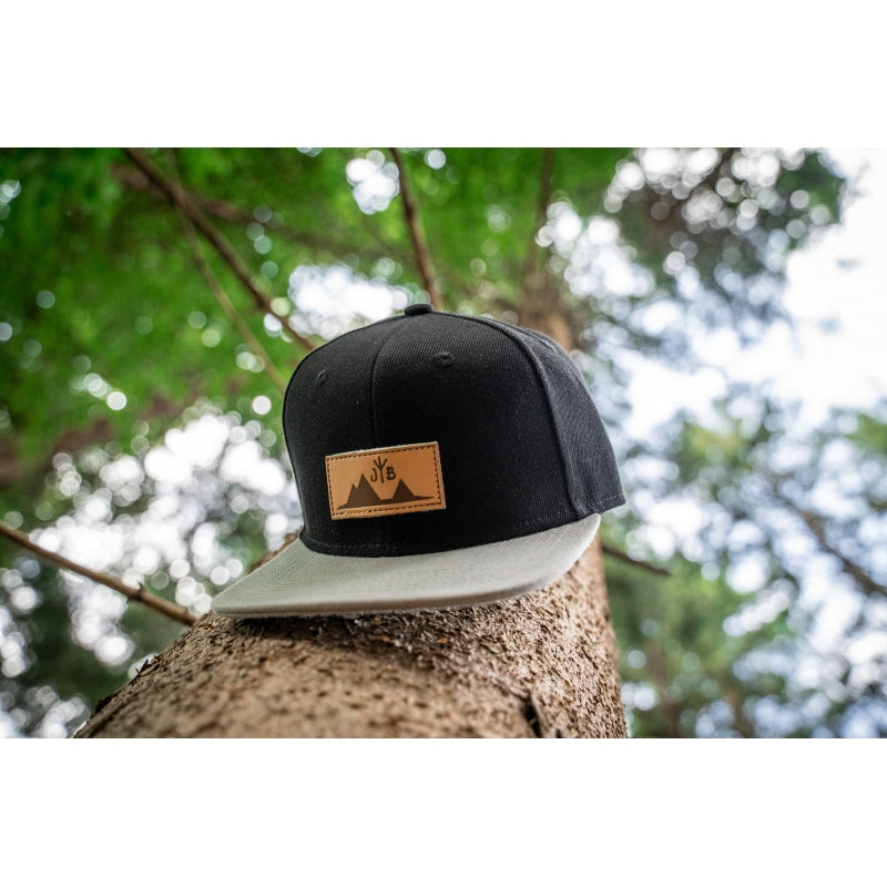 Snapback-Cap von Jumping Bird in Schwarz-Grau mit geprägtem Lederoptik-Patch vorn und seitlichem Logostick